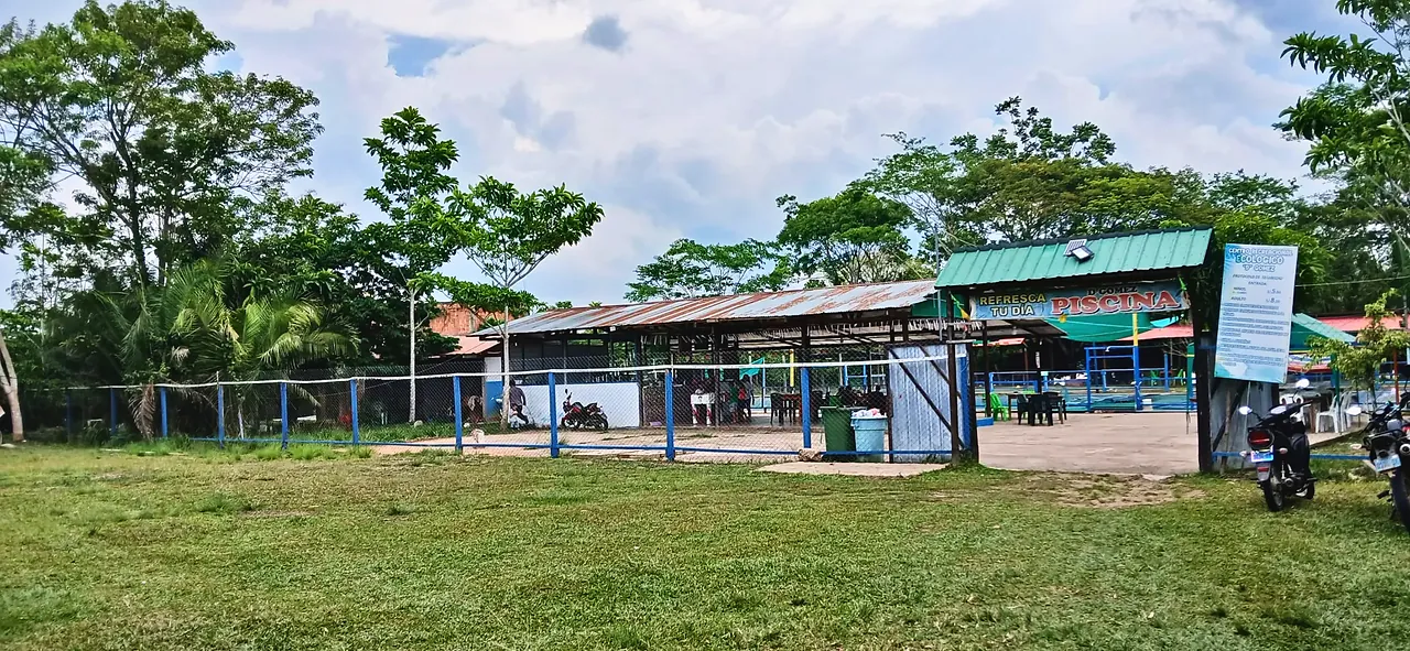 Entrada del centro recreacional vista desde el campo, con el letrero «Refresca tu día – Piscina».