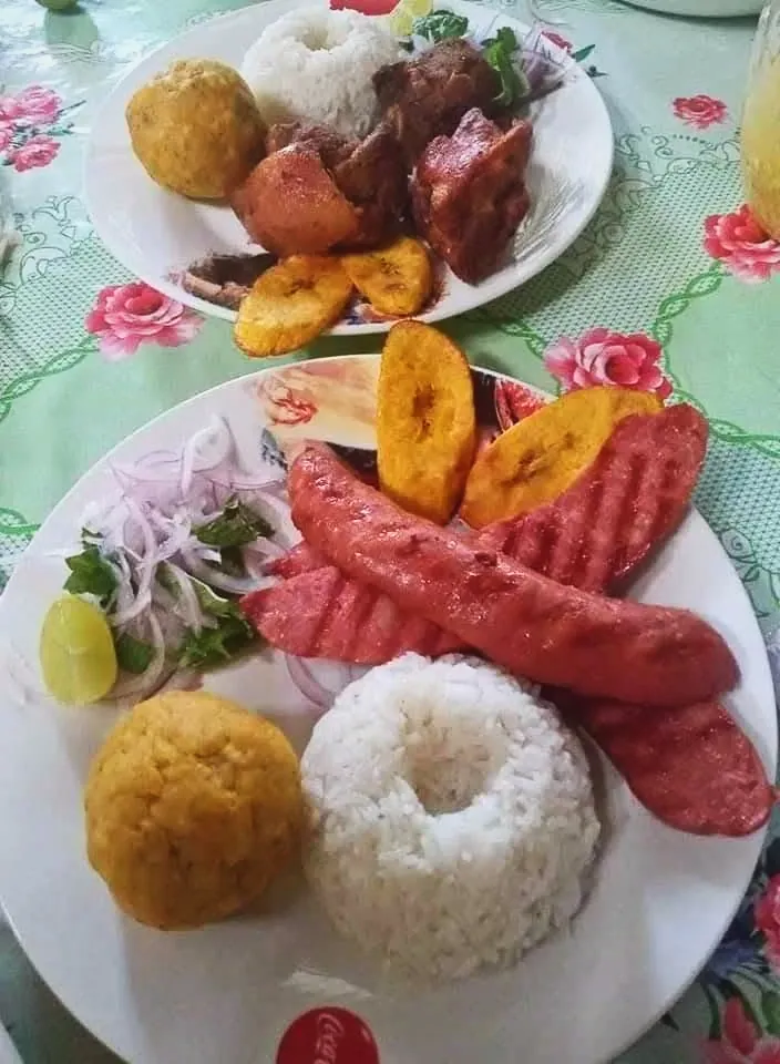 Dos platos de fin de semana con carnes fritas y a la parrilla, arroz, plátano frito, una bola dorada y sarsa de cebolla con limón.